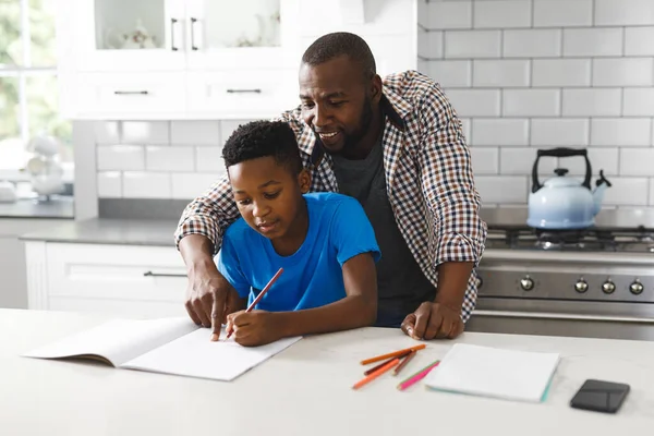 笑非洲裔美国父亲和他的儿子在厨房 一起做作业 家庭呆在家里的时间 — 图库照片