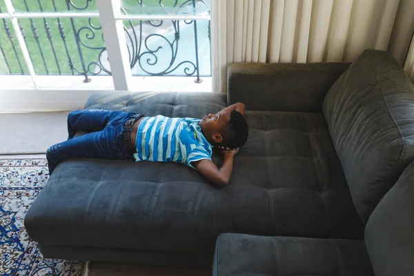 富有独立精神的非洲裔美国男孩躺在沙发上 凝视着客厅的窗外 独自呆在家里 — 图库照片