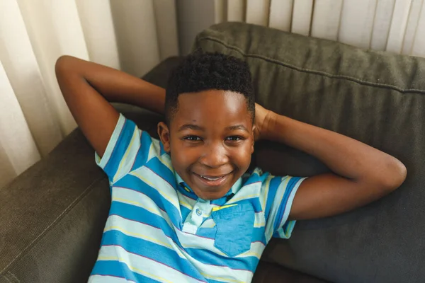 一个面带微笑的非洲裔美国男孩躺在客厅沙发上的画像 独自呆在家里 — 图库照片