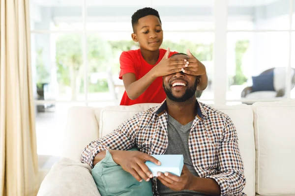 Улыбающийся Африканский Американец Отец Открывает Подарок Своего Сына Пока Закрывает — стоковое фото