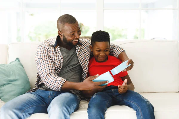 Šťastný Africký Americký Otec Otevírá Dárek Svého Syna Usmívá Obýváku — Stock fotografie