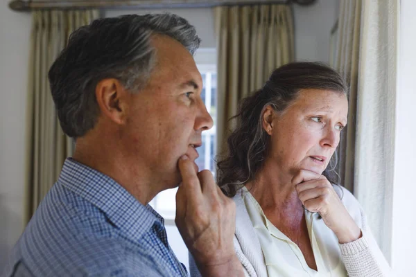 Thoughtful Senior Caucasian Couple Standing Next Window Holding Chins Retirement — Stock Photo, Image