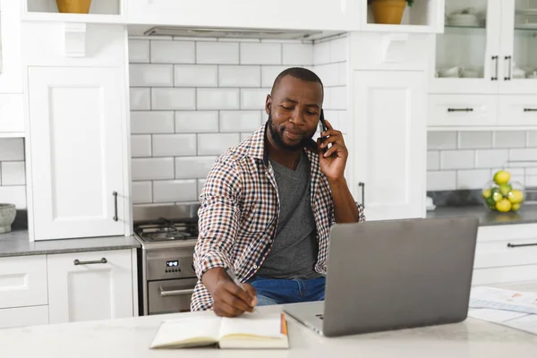 Afrykański Amerykanin Siedzi Kuchni Pracuje Laptopie Smartfonie Zdalna Praca Domu — Zdjęcie stockowe