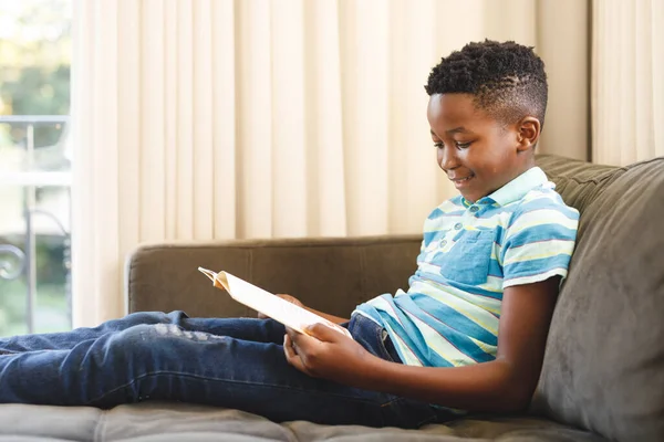 Smiling African American Boy Reading Book Sitting Couch Living Room — Stock Photo, Image