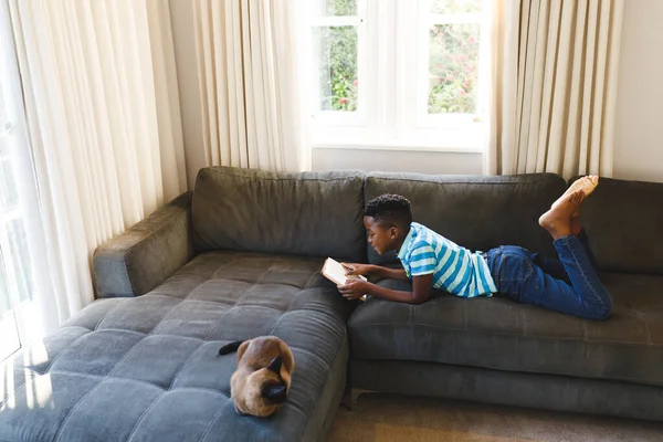 Niño Afroamericano Leyendo Libro Acostado Sofá Con Gato Sala Estar — Foto de Stock