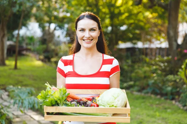 庭に立つ笑顔の白人女性の肖像新鮮な有機野菜の箱を保持 園芸や自給自足 家庭用品の栽培など — ストック写真