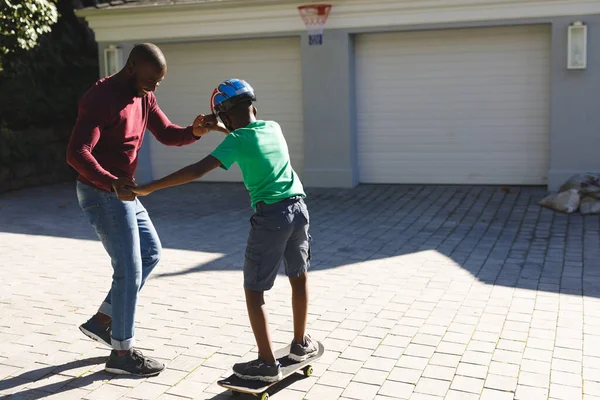 Африканський Батько Американець Посміхається Допомагає Синові Балансувати Скейтборді Саду Сім — стокове фото