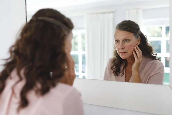 浴室のシニア白人女性は 鏡の中で彼女の顔を見て 退職生活と高齢化の過程は — ストック写真