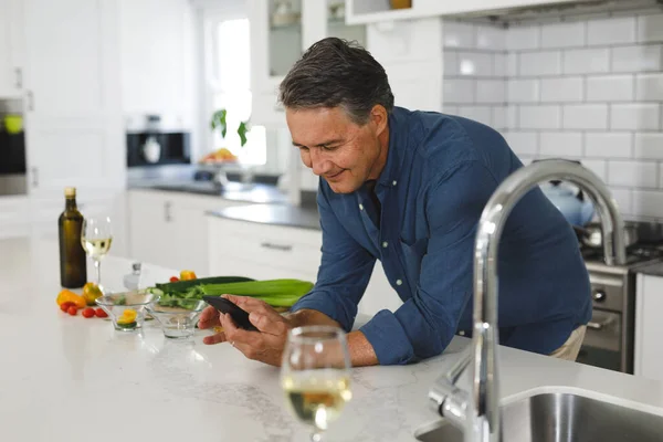 現代のキッチンで笑顔のシニア白人男性 スマートフォンを使用して 引退後の生活や家で過ごす時間 — ストック写真