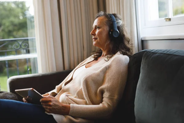 Oturma Odasında Oturan Kulaklık Takan Tablet Kullanan Mutlu Beyaz Kadın — Stok fotoğraf