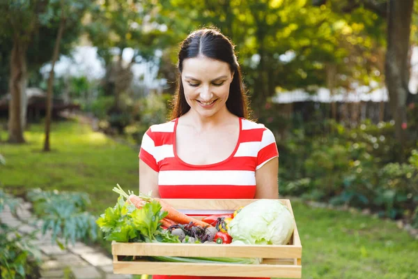 庭に立つ笑顔の白人女性新鮮な有機野菜の箱を持っています 園芸や自給自足 家庭用品の栽培など — ストック写真