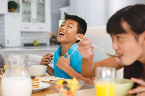 笑着亚洲兄弟和姐姐一起坐在早餐桌旁吃饭 家庭在家里共进午餐 — 图库照片