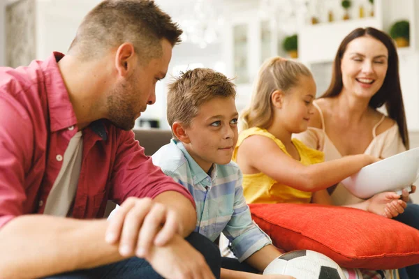 幸せな白人の両親 娘と息子がソファに座ってテレビでサッカーの試合を見て話しています 家族の娯楽と余暇を一緒に家で — ストック写真