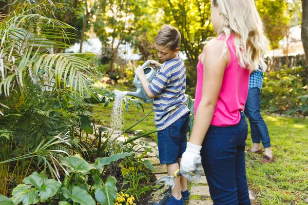 母親と父親を背景に庭の白人の息子と娘の散水植物 ご家族でゆっくりとお庭でお過ごしください — ストック写真