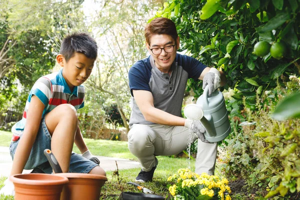 幸せなアジアの父と息子の笑顔 手袋や散水植物を一緒に庭で身に着けている 家庭菜園での余暇 — ストック写真