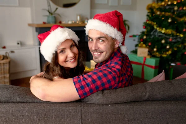 快乐的加卡人夫妇戴着圣诞礼帽 坐在沙发上 圣诞节 节日和通信技术 — 图库照片