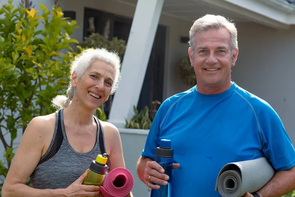 ヨガマットを持ってカメラを見ている幸せな白人のシニアカップル 家庭や庭で積極的かつ健康的な退職生活を — ストック写真