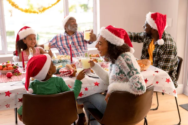 サンタの帽子をかぶった幸せなマルチ世代の家族は クリスマスの食事をしています クリスマスの時間と祭りを一緒に家で — ストック写真