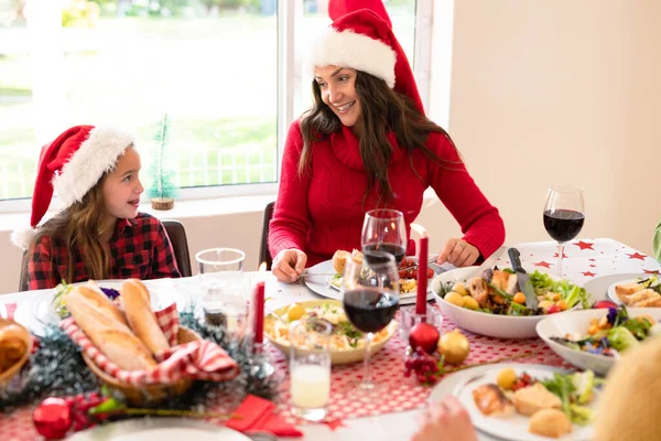 Noel Baba Şapkası Takan Mutlu Anne Kız Noel Masasında Oturuyorlar — Stok fotoğraf