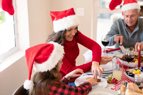 クリスマスの食事を持つサンタの帽子を身に着けている白人の複数世代の家族 クリスマスの時間と祭りを一緒に家で — ストック写真