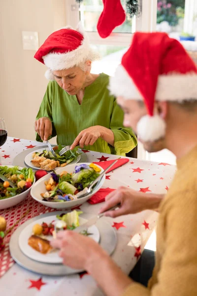 Schoonmoeder Schoonzoon Met Kerstmutsen Aan Tafel Eten Familie Kersttijd Festiviteit — Stockfoto