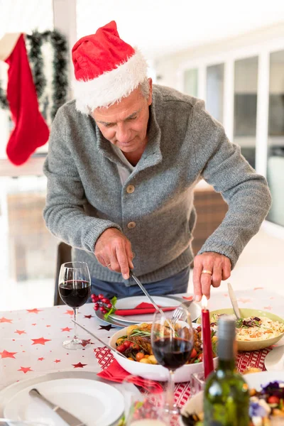 クリスマスのテーブルで食べ物を切る幸せな白人の先輩 クリスマスの時間と祭りを一緒に家で — ストック写真