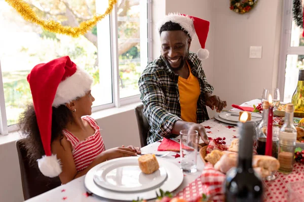 幸せなアフリカ系アメリカ人の父と娘がクリスマステーブルで話しています クリスマスの時間と祭りを一緒に家で — ストック写真