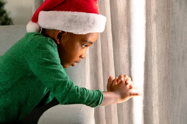 Rapaz Afro Americano Usar Chapéu Pai Natal Olhar Pela Janela — Fotografia de Stock