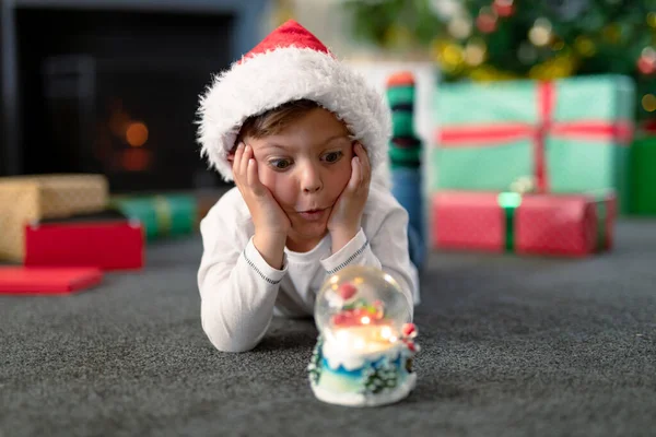 Chico Caucásico Sorprendido Vistiendo Sombrero Santa Mirando Bola Nieve Navidad — Foto de Stock