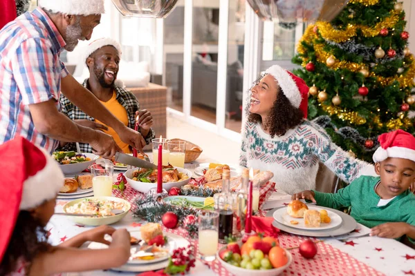 幸せなアフリカ系アメリカ人の複数世代の家族はクリスマスの食事を持っている クリスマスの時間と祭りを一緒に家で — ストック写真