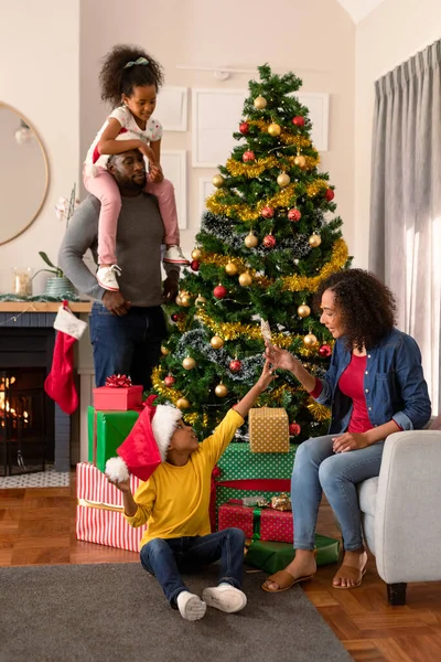 サンタの帽子をかぶっている幸せなアフリカ系アメリカ人の父親とクリスマスツリーを飾る娘 家庭でのクリスマスやお祭りや伝統 — ストック写真