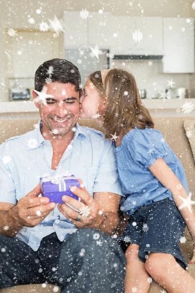 Girl kissing father holding gift box on sofa — Stock Photo, Image