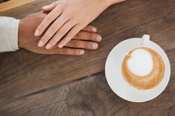 Paar hält Händchen neben Cappuccino — Stockfoto