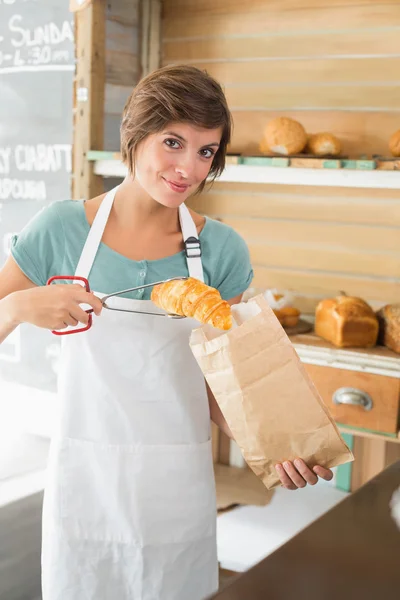 Jolie serveuse mettant croissant dans un sac en papier — Photo