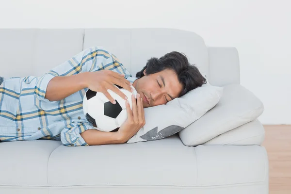 Tifoso di calcio che abbraccia palla sul divano — Foto Stock