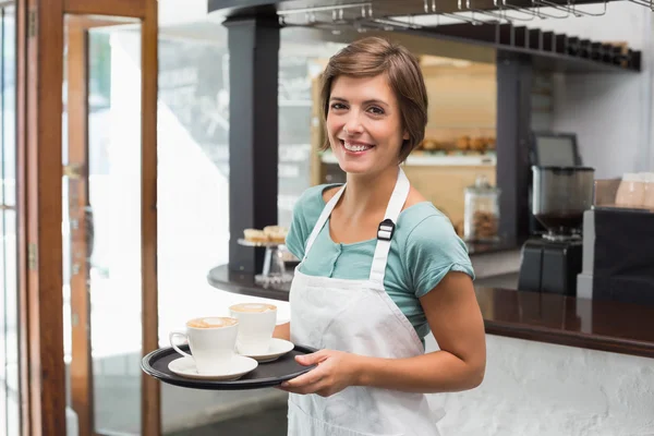 Bastante barista sonriendo a la cámara sosteniendo bandeja —  Fotos de Stock