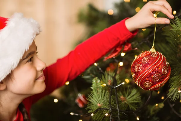 Festliches kleines Mädchen hängt eine Weihnachtsdekoration auf — Stockfoto