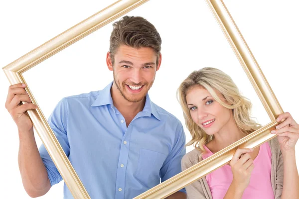 Casal atraente sorrindo para a câmera através do quadro de imagem — Fotografia de Stock