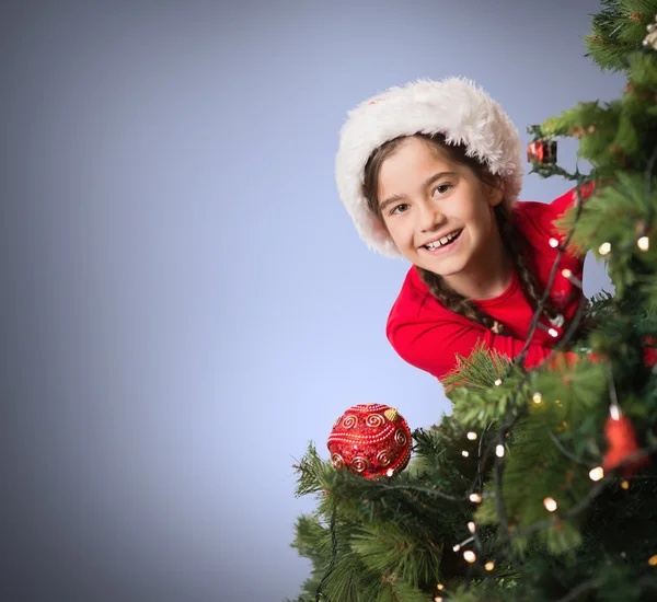 Ragazza festiva guardando da dietro l'albero di Natale — Foto Stock