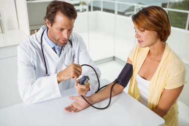 Doctor checking blood pressure of woman at medical office clipart