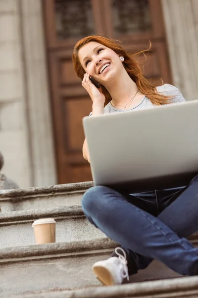 Leende tjej ringer med sin mobiltelefon och använder bärbar dator — Stockfoto