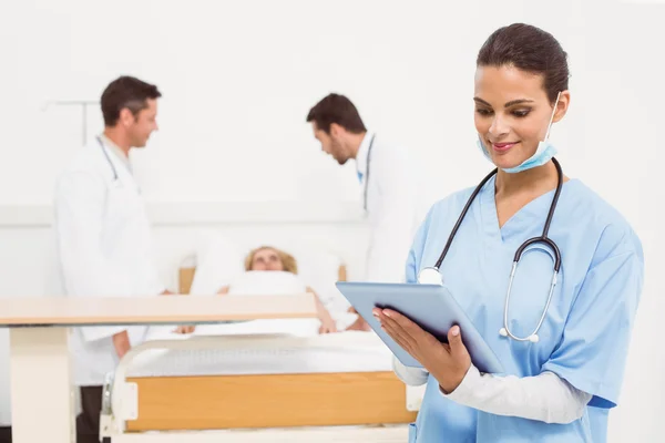 Γιατρός χρησιμοποιώντας ψηφιακή δισκίο με συναδέλφους και ασθενής πίσω από — Φωτογραφία Αρχείου