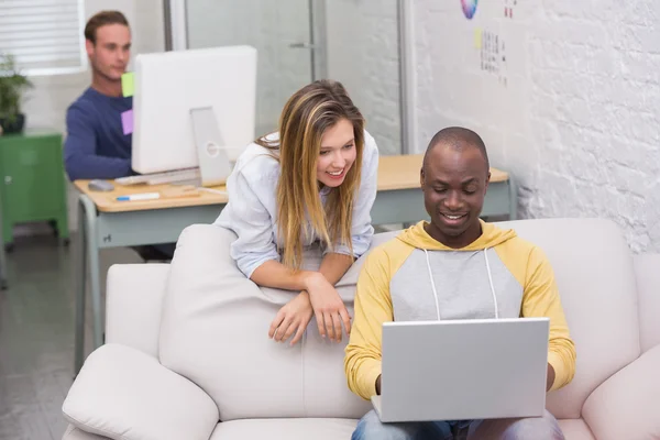 Collèges occasionnels utilisant un ordinateur portable sur le canapé dans le bureau — Photo