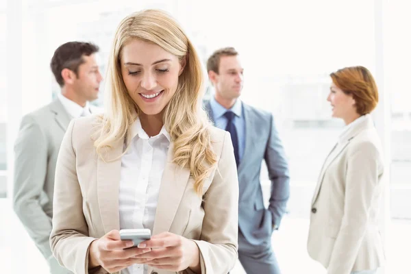 Businesswoman text messaging with colleagues in meeting behind — Stock Photo, Image