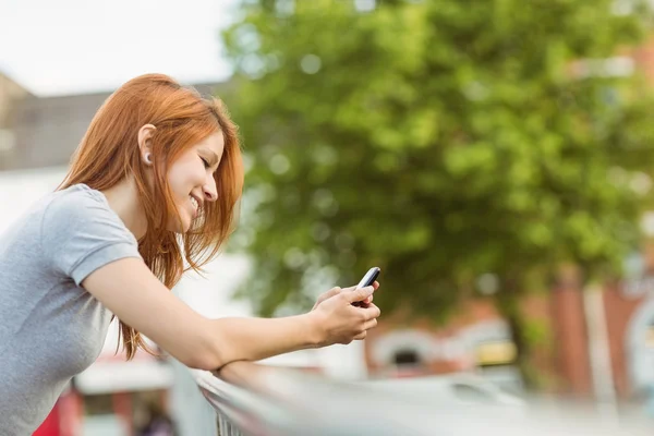 Ruiva sorridente com seu telefone celular enviando uma mensagem — Fotografia de Stock