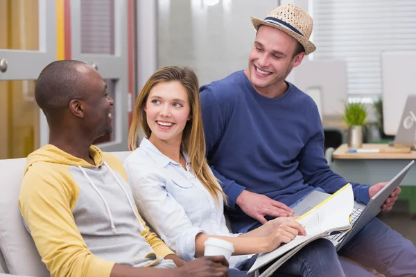 Collèges occasionnels utilisant un ordinateur portable sur le canapé dans le bureau — Photo