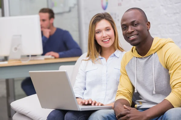 Casual colleagues using laptop on couch in office — Stock Photo, Image