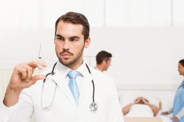 Médico segurando injeção com colegas e paciente atrás — Fotografia de Stock