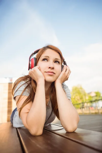 Pretty redhead lying on bench listening to music — Stock Photo, Image