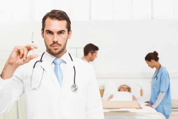 Arzt hält Spritze mit Kollegen und Patient im Rücken — Stockfoto